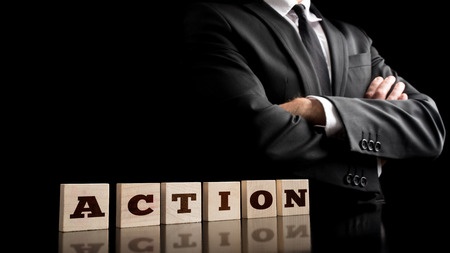 42851664 - businessman in a strong confident pose standing next to six wooden cubes spelling action in a conceptual image of business vision and determination.